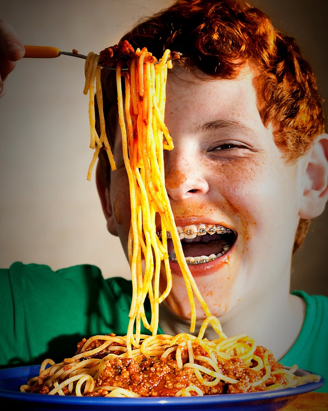 A boy with braces eats spaghetti marinara.